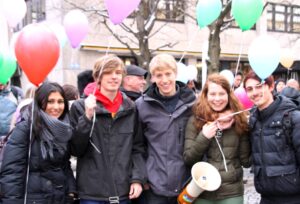 5 junge Menschen mit Luftballons und Mikrophon auf einer Demonstration
