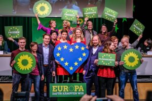 Grünen Politiker halten Schilder mit Sonnenblumen, Europaflagge und Forderungen nach Klimaschutz, Demokratie und Gerechtigkeit hoch.